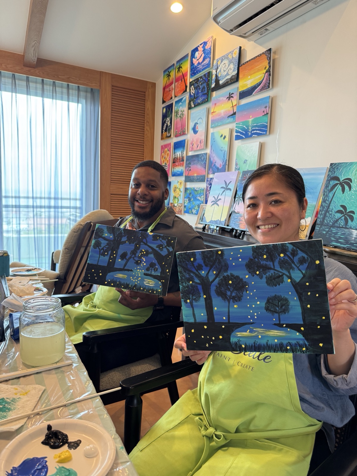 Two Pinto Beetle guests holding finished firefly forest paintings in the studio