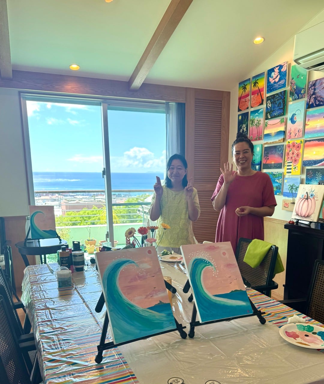 Two Pinto Beetle guests standing with finished pink moon wave paintings in the ocean-view studio