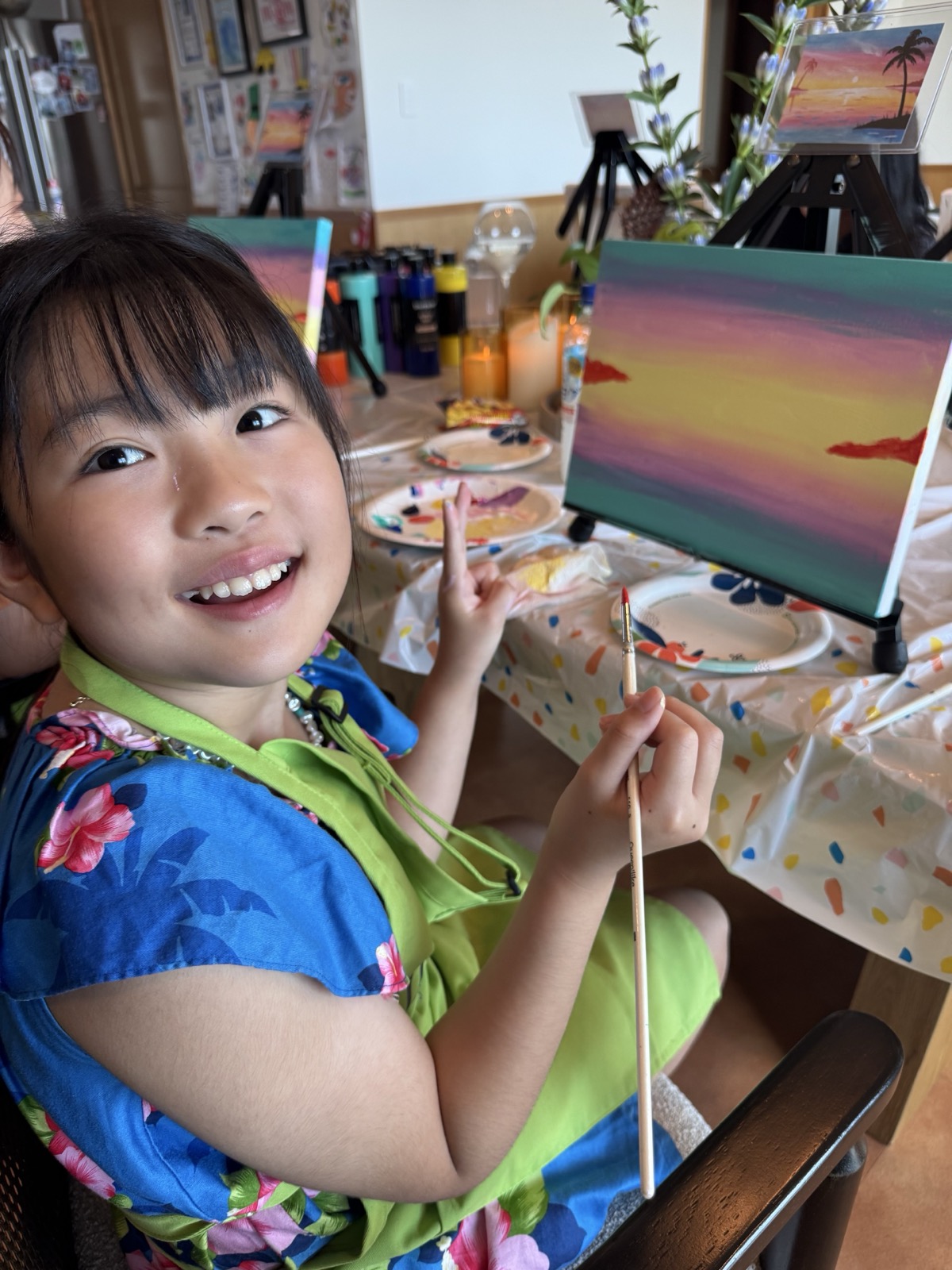 Young Pinto Beetle guest smiling beside her Sunset Paradise painting in progress