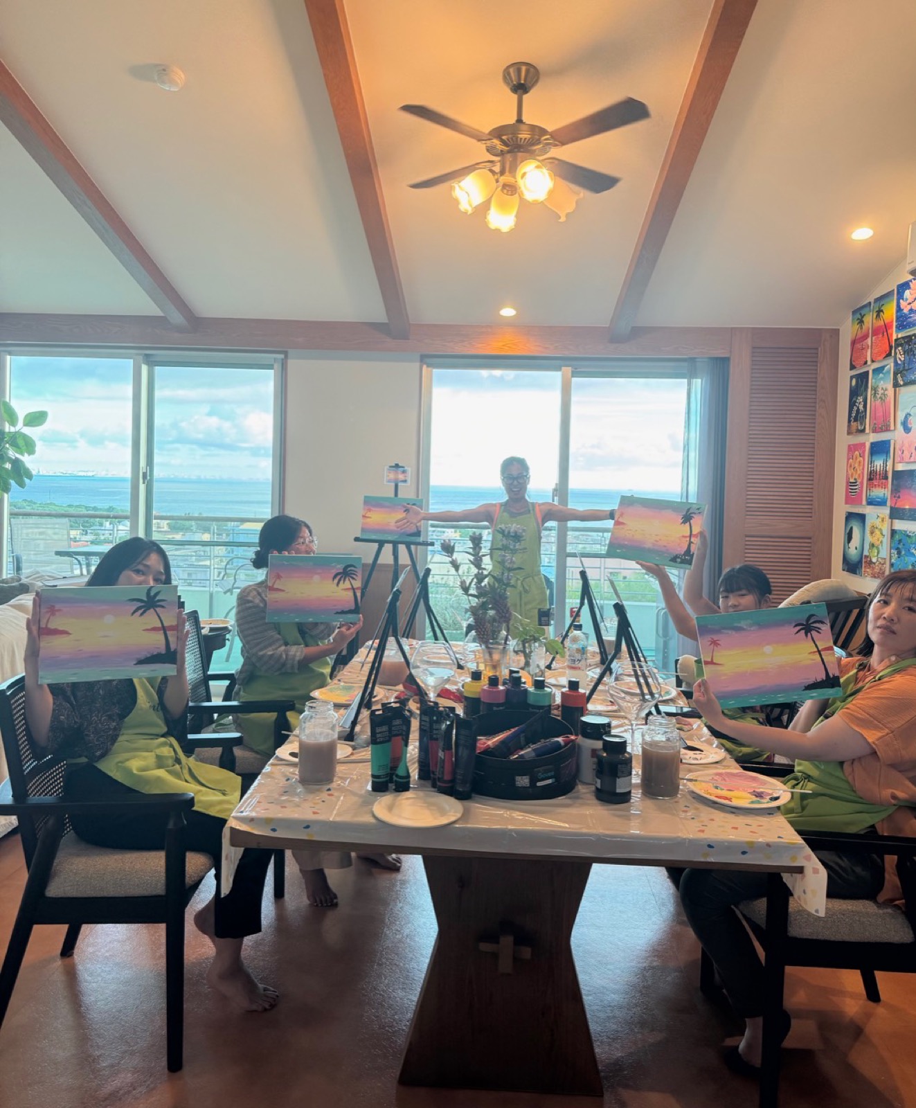 Pinto Beetle guests holding Sunset Paradise paintings around the ocean-view studio table